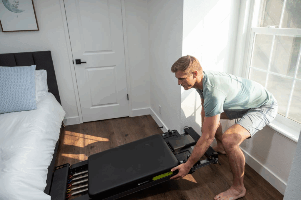 Мужчина настраивает тренажёр Metro IQ Reformer в домашней обстановке.
